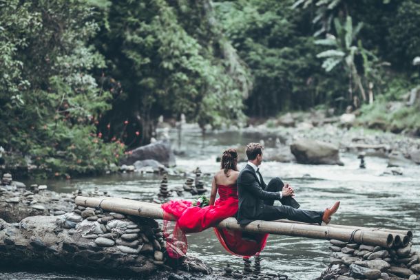 a couple outside sitting over a river in formal clothes
