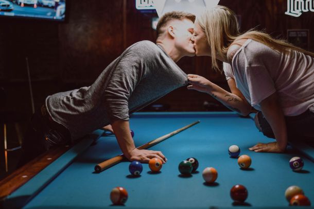 a couple kissing over a pool table indoors