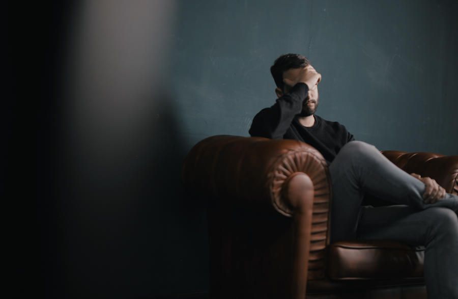 a man sitting on a couch stressed holding his head