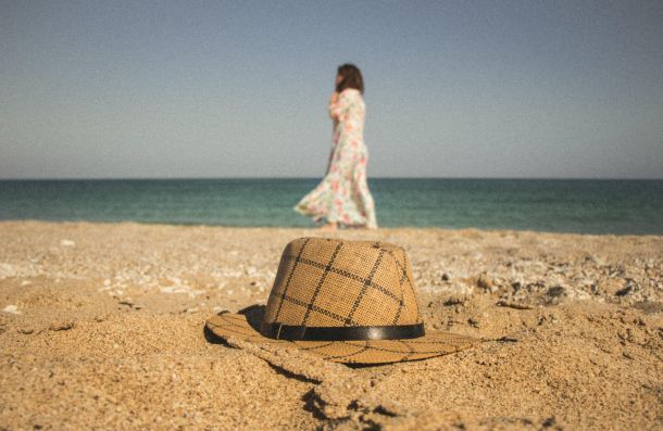 woman walking on a beach outside with a hat on the sand