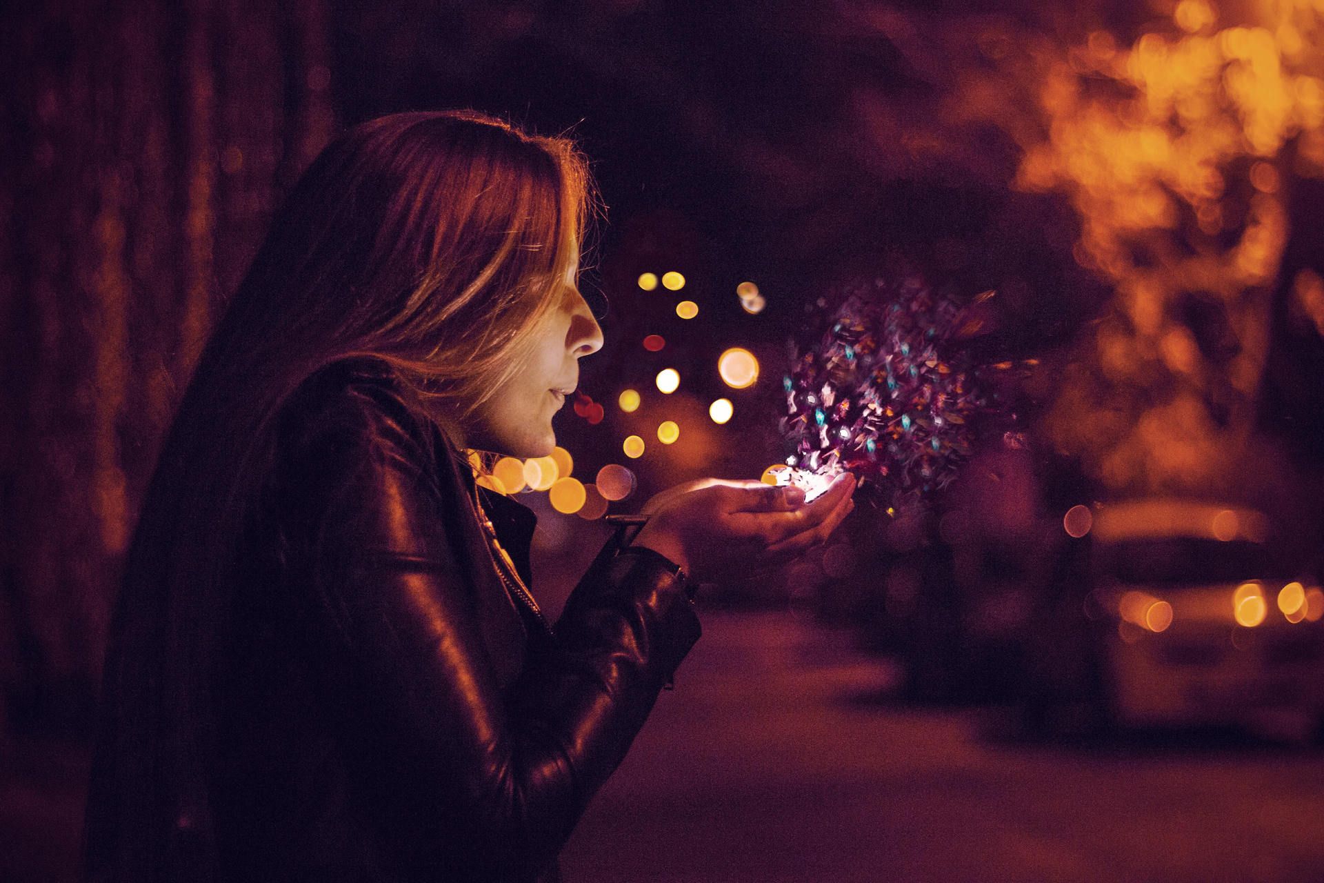 Woman outside at night blow lighted dust out of her cupped hands