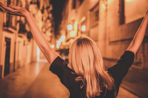 woman with arms in the air outside at night in an alley